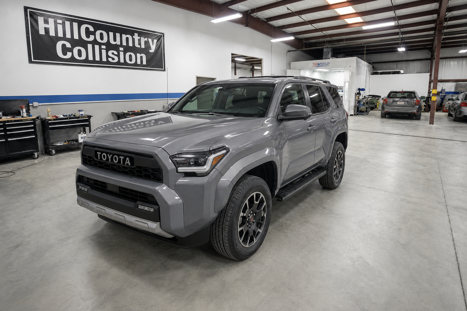 Gray Toyota SUV parked inside a collision repair shop with a HillCountry Collision banner on the wall.